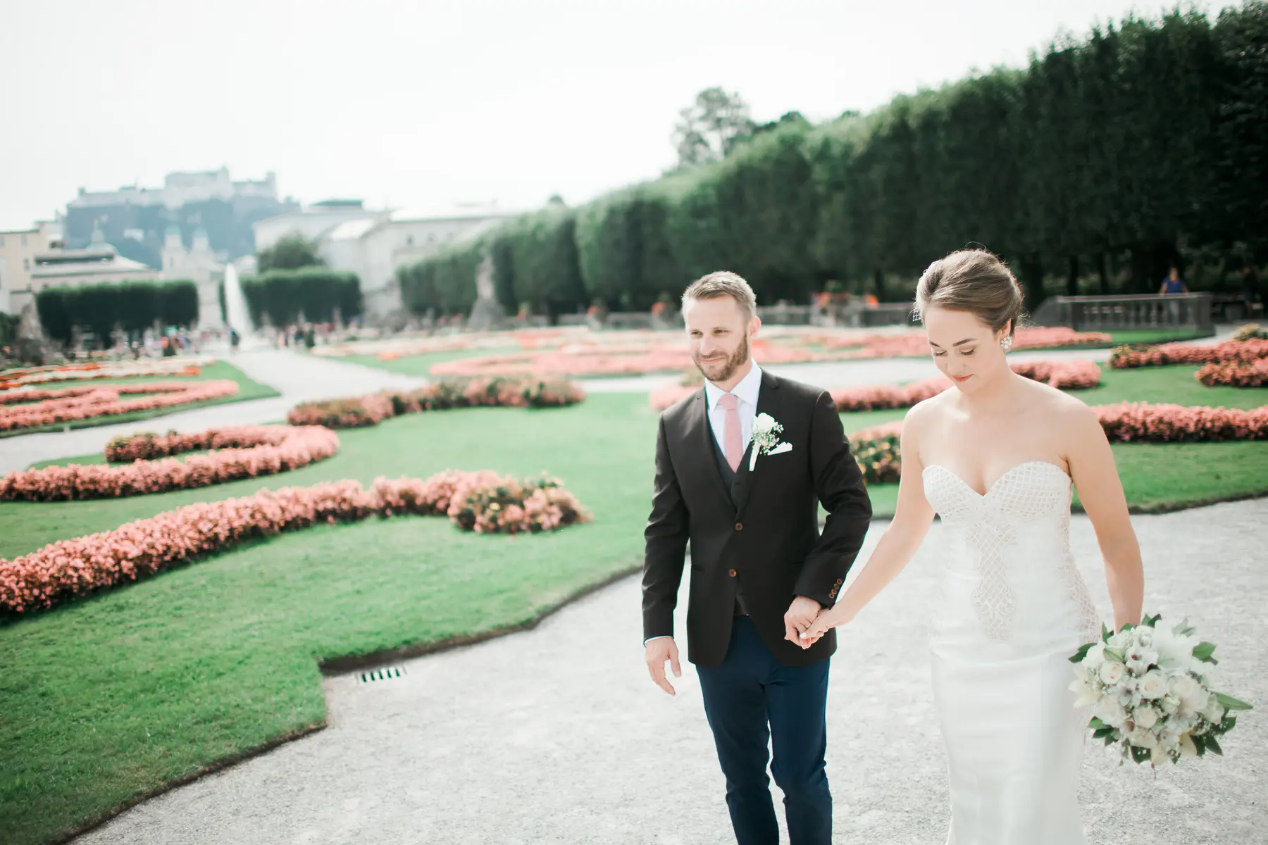 Exklusive Destination Wedding Fotografie in Salzburg: Brautpaar-Porträt im Mirabellgarten mit Blick auf die Festung Hohensalzburg und den Salzburger Dom. Majestätische Kulisse für zeitlose Hochzeitsfotos in Österreich. Hochwertige Hochzeitsreportage von Still and Motion Pictures für internationale Paare.