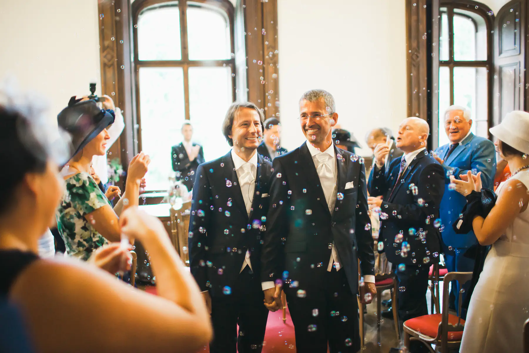 Authentische Hochzeitsreportage in Österreich: Zwei Bräutigame feiern ihren Auszug inmitten von Seifenblasen. Einzigartiger Moment voller Freude und natürlicher Emotionen. Moderne, ungestellte Hochzeitsfotografie und Storytelling für gleichgeschlechtliche Hochzeiten von Marek & Klára. Love wins in Wien.