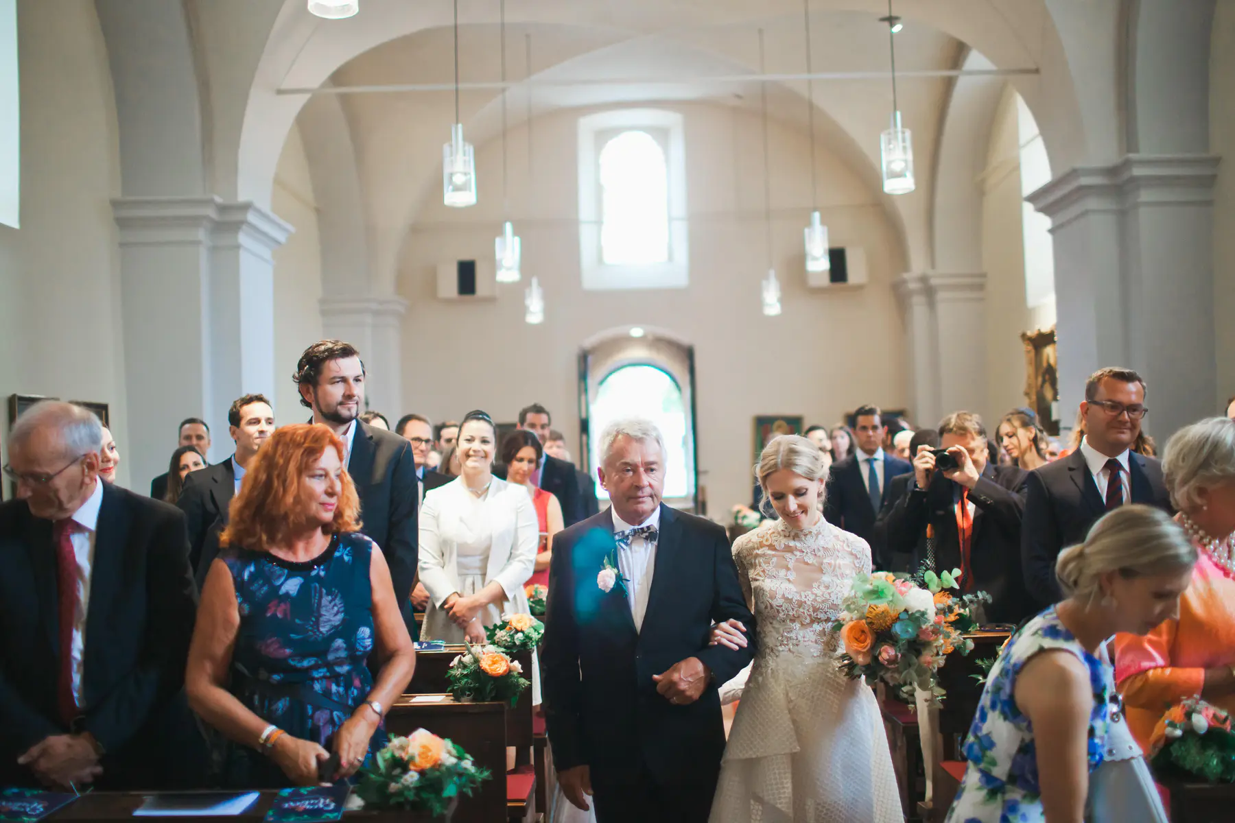 Kirchliche Trauung in Wien: Braut im Spitzenkleid am Arm ihres Vaters beim Einzug in die Pfarrkirche St. Jakob (Heiligenstadt). Authentische Hochzeitsreportage und emotionale Momente während der Zeremonie. Professionelle Hochzeitsfotografie im 19. Bezirk von Still and Motion Pictures.