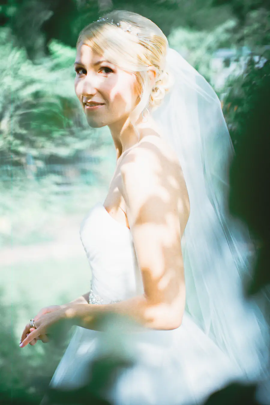 A bride in a white wedding dress and veil smiles as she looks to her left. Captured on Fuji Film PRO 400H.