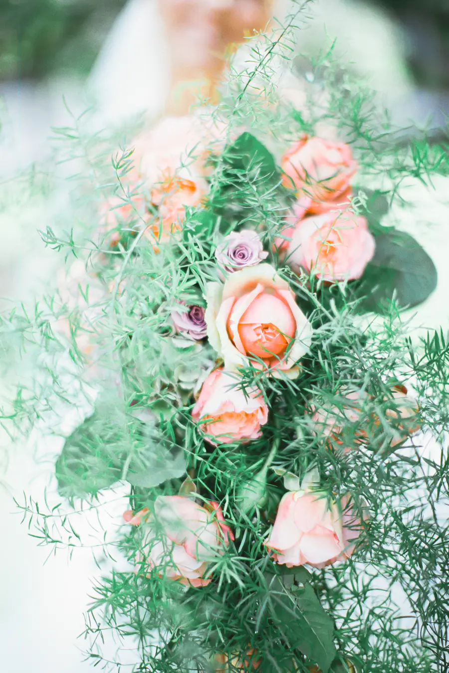Captured on Fuji Film PRO 400H.A close-up, soft-focus shot of a floral arrangement of pink and peach roses with delicate green foliage.