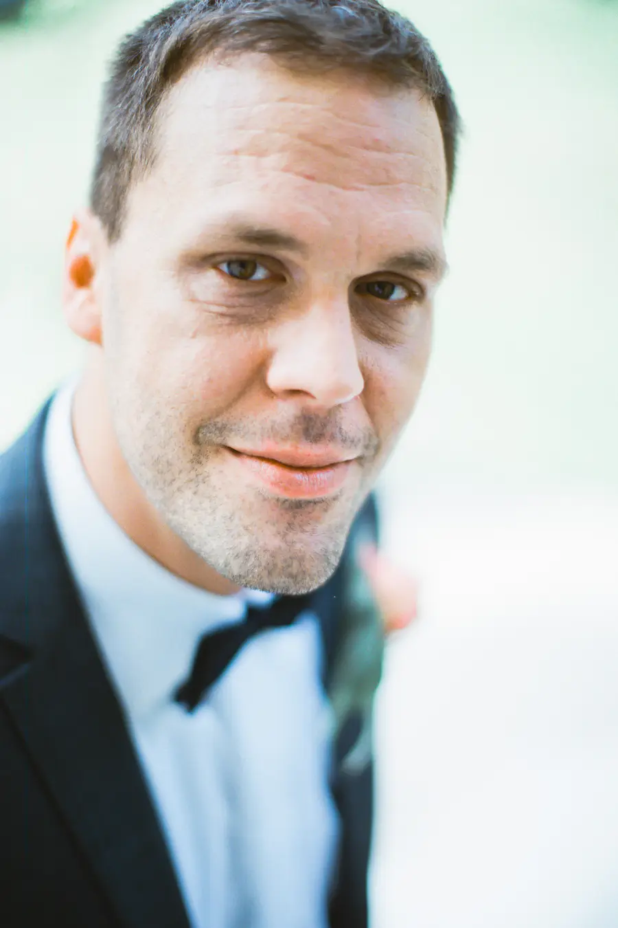 Captured on Fuji Film PRO 400H.A close-up, soft-focus shot of a man wearing a black suit, white shirt, and black bow tie.