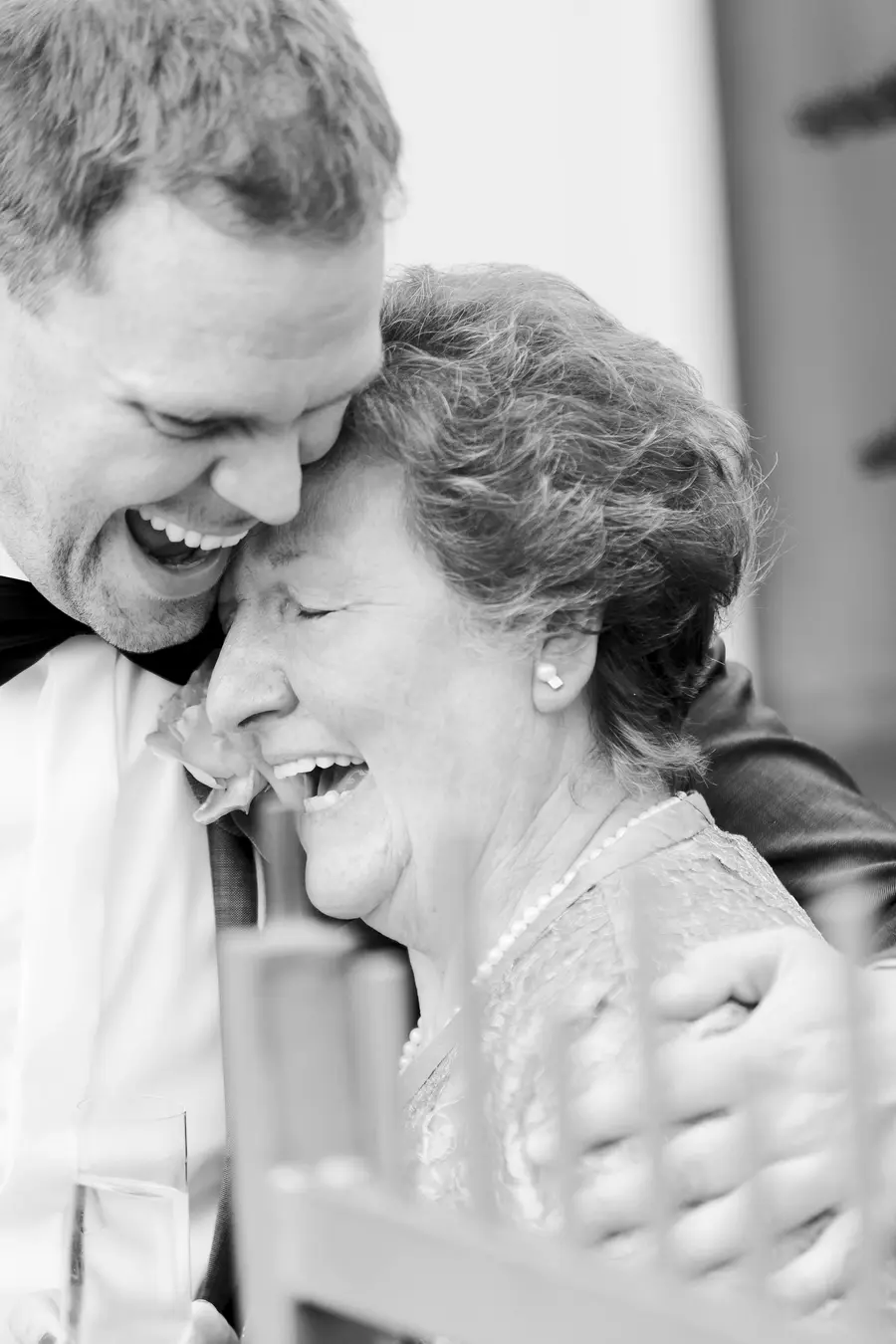 A man in a tuxedo laughs heartily while hugging an older woman his mam who is also laughing.Marek & Klara reportage Wedding photo Vienna: