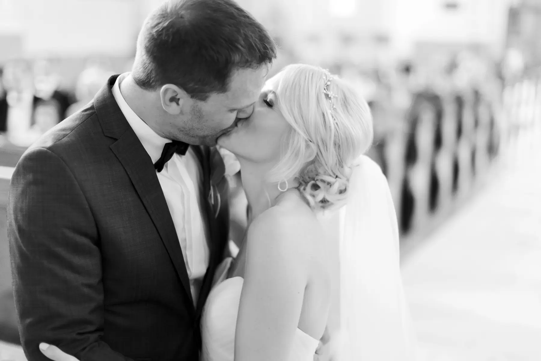 A groom in a tuxedo and a bride in a strapless wedding dress share a kiss.