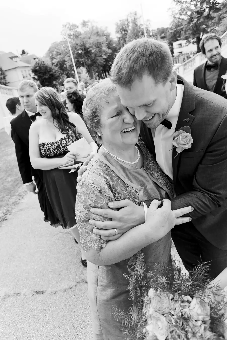 A smiling groom hugs his mother, who is also smiling, on a wedding day.