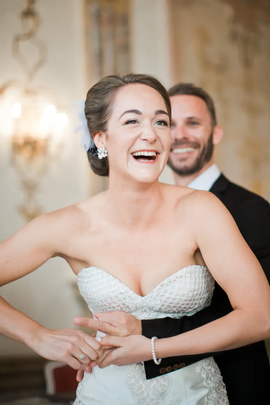 A laughing bride in a strapless white gown is embraced by a smiling groom in a black suit.Raw and Real Wedding Moments Salzburg