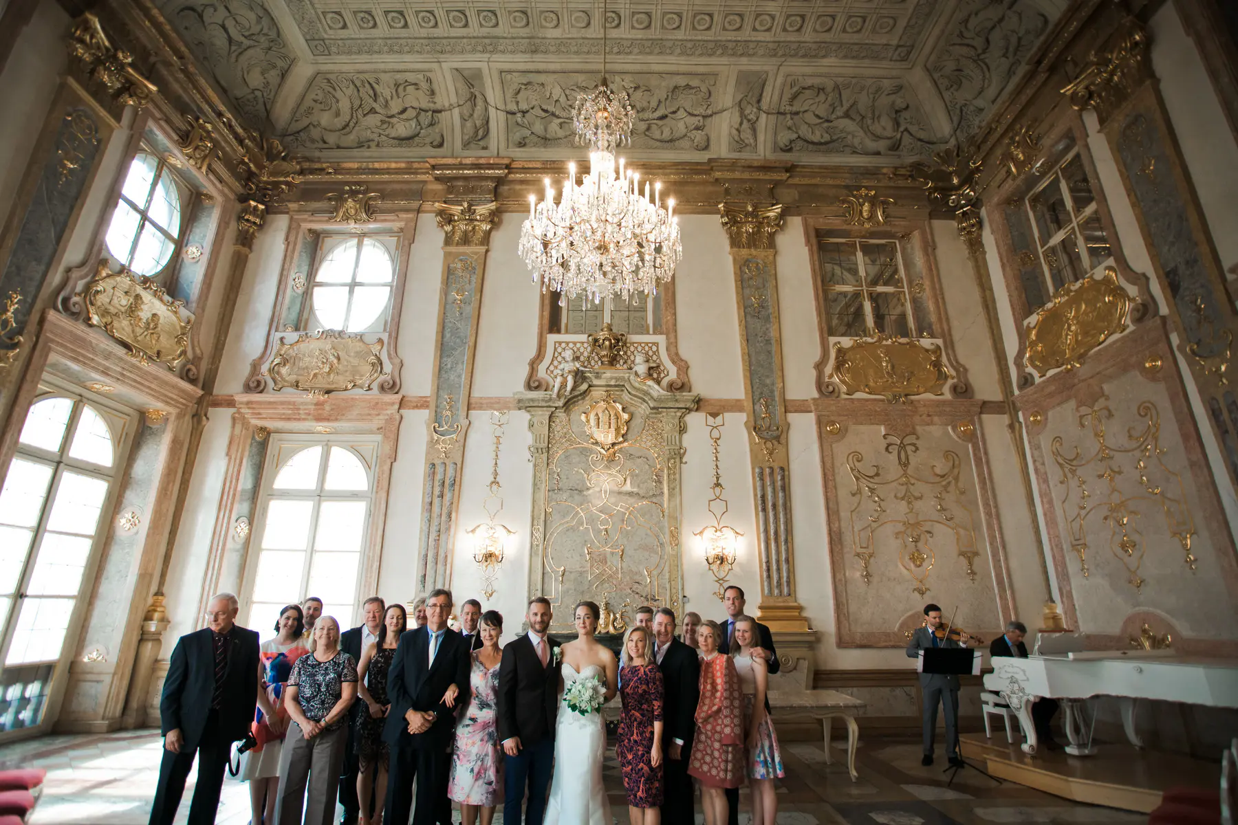 Wide shot of a bride and groom standing in the luxurious Marble Hall of Mirabell Palace in Salzburg, showcasing the grand Baroque architecture and emotional atmosphere after the ceremony.