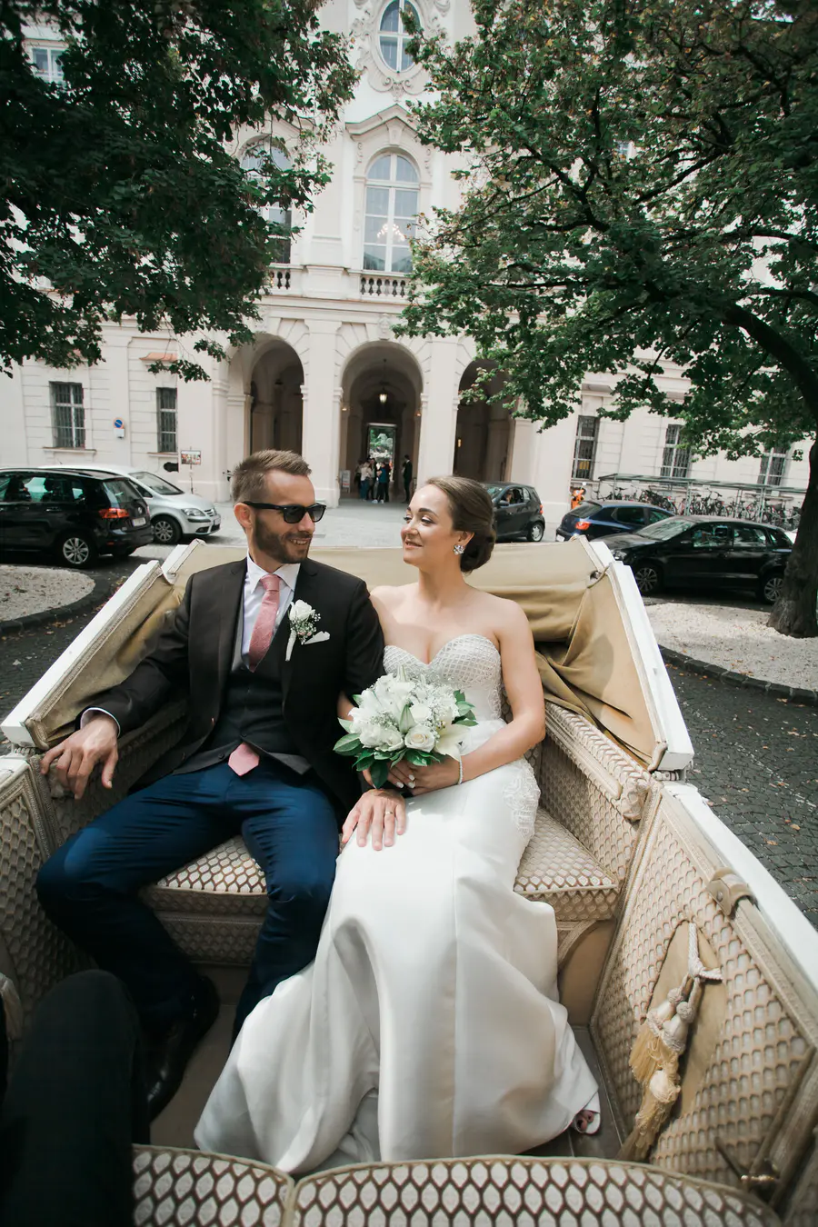 A scenic shot of the wedding couple in a traditional horse-drawn carriage passing through the sunny streets of Salzburg's Old Town.