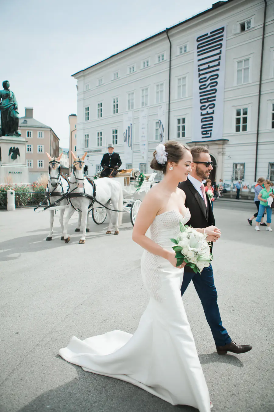 European Elopement Photographer.A natural storytelling frame of the couple walking on the open square in front of the Salzburg Museum, surrounded by the city's historic charm.