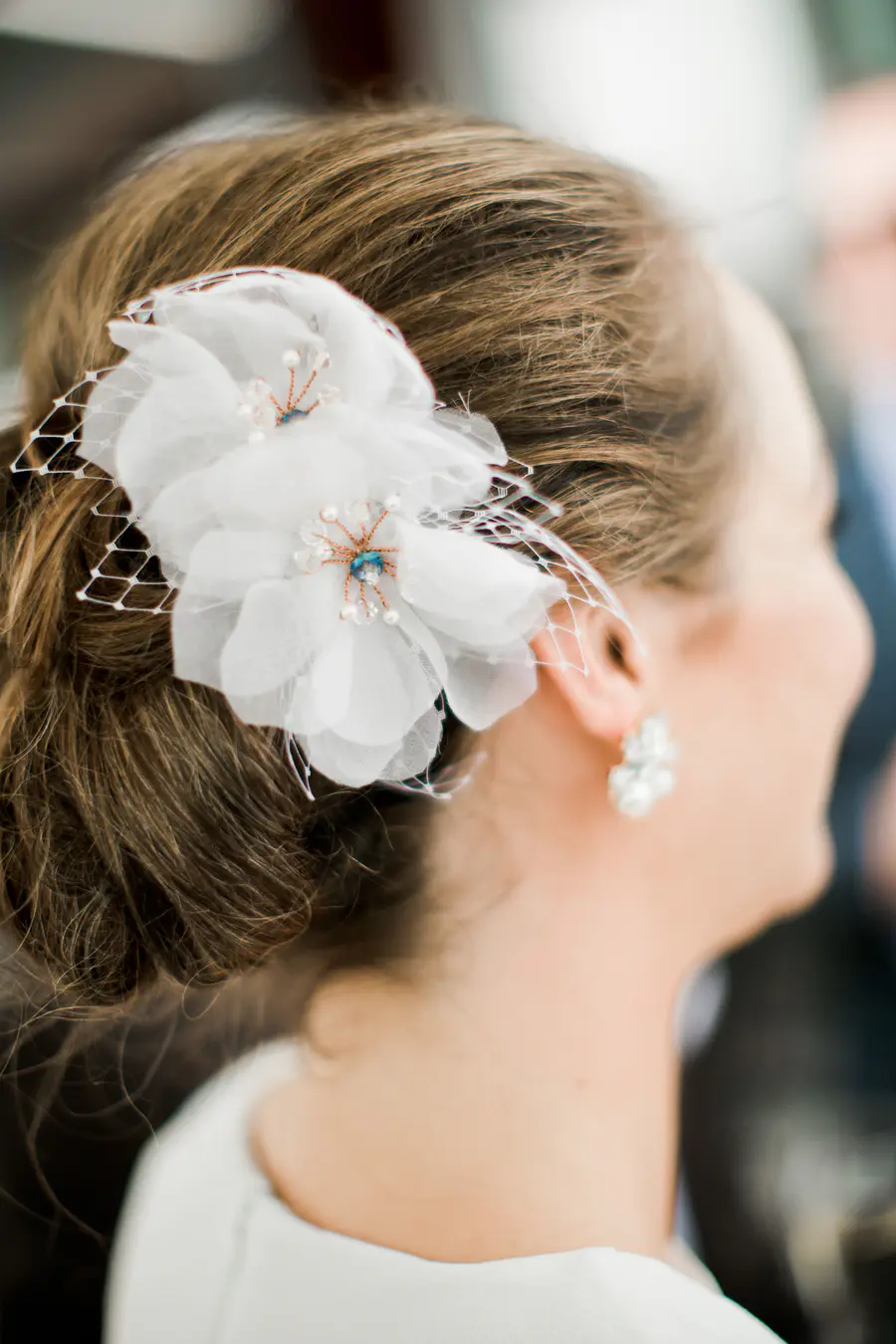 A close-up portrait of a bride in a white lace dress, looking down at an orange and pink bouquet.