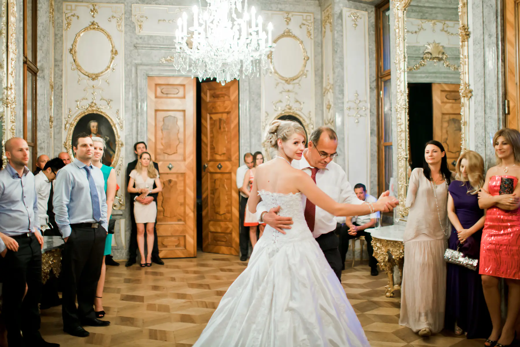 A bride and her father dance in a grand ballroom, surrounded by wedding guests at Schloss Hetzendorf