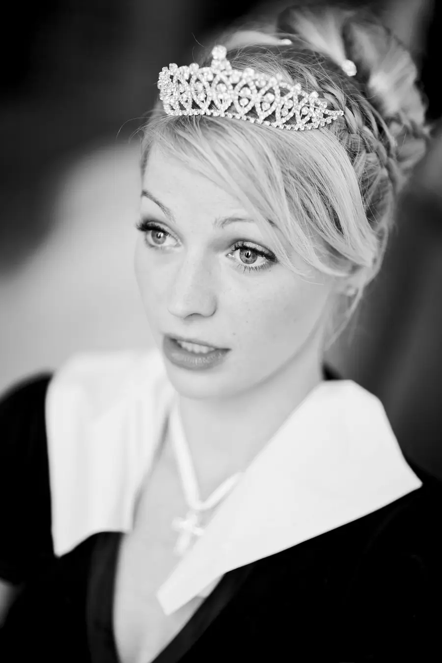 A close-up, black and white portrait of a young bride wearing a jeweled tiara and a white collared garment.
