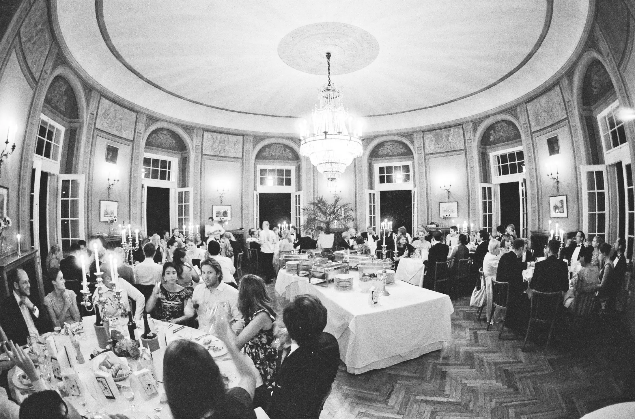 Analoque wedding photography shot on Ilford Delta 3200 Pro - Crystal chandelier hang above a wedding reception hall filled with guests seated atttables.