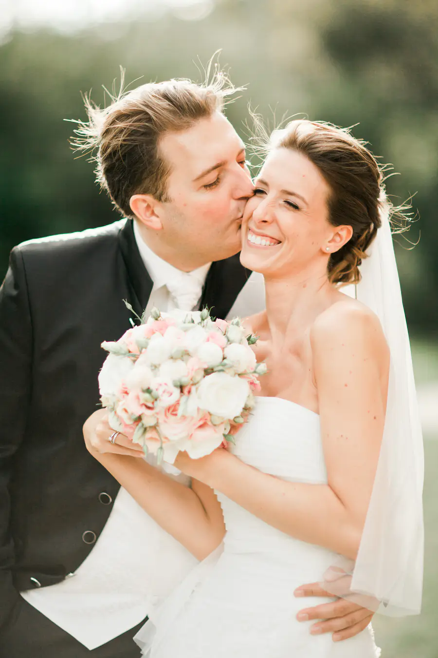 Natural wedding photography Vienna – Groom kissing bride with pink bouquet, authentic photojournalistic moment by Stillandmotionpictures duo.