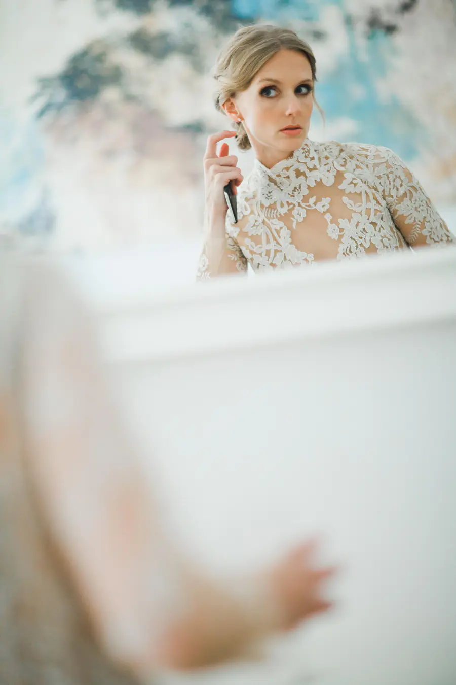 A blonde woman in a white lace dress sprays perfume on her wrist.