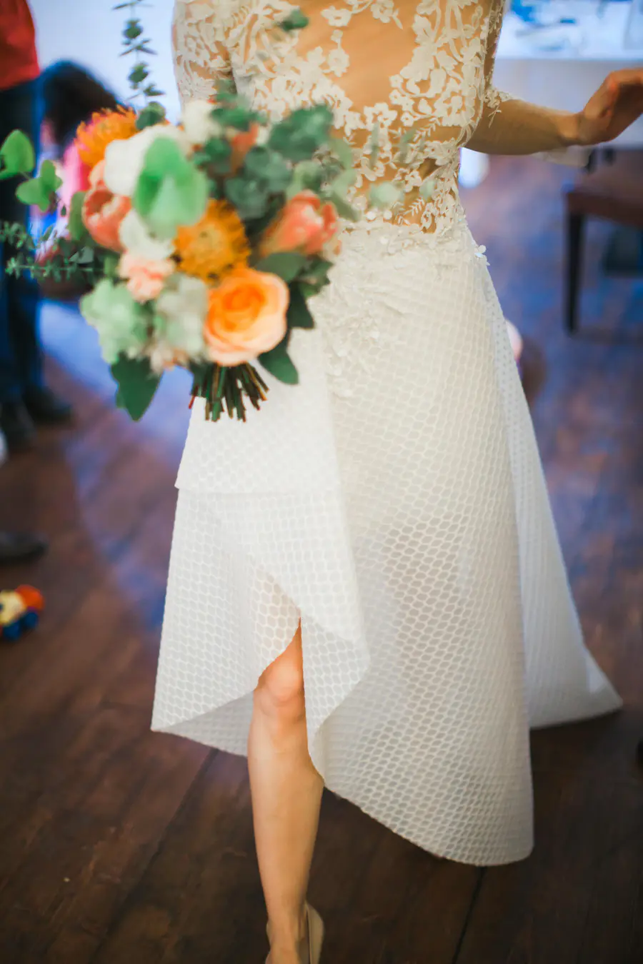 A bride in a white lace wedding dress holds a colorful bouquet of flowers.