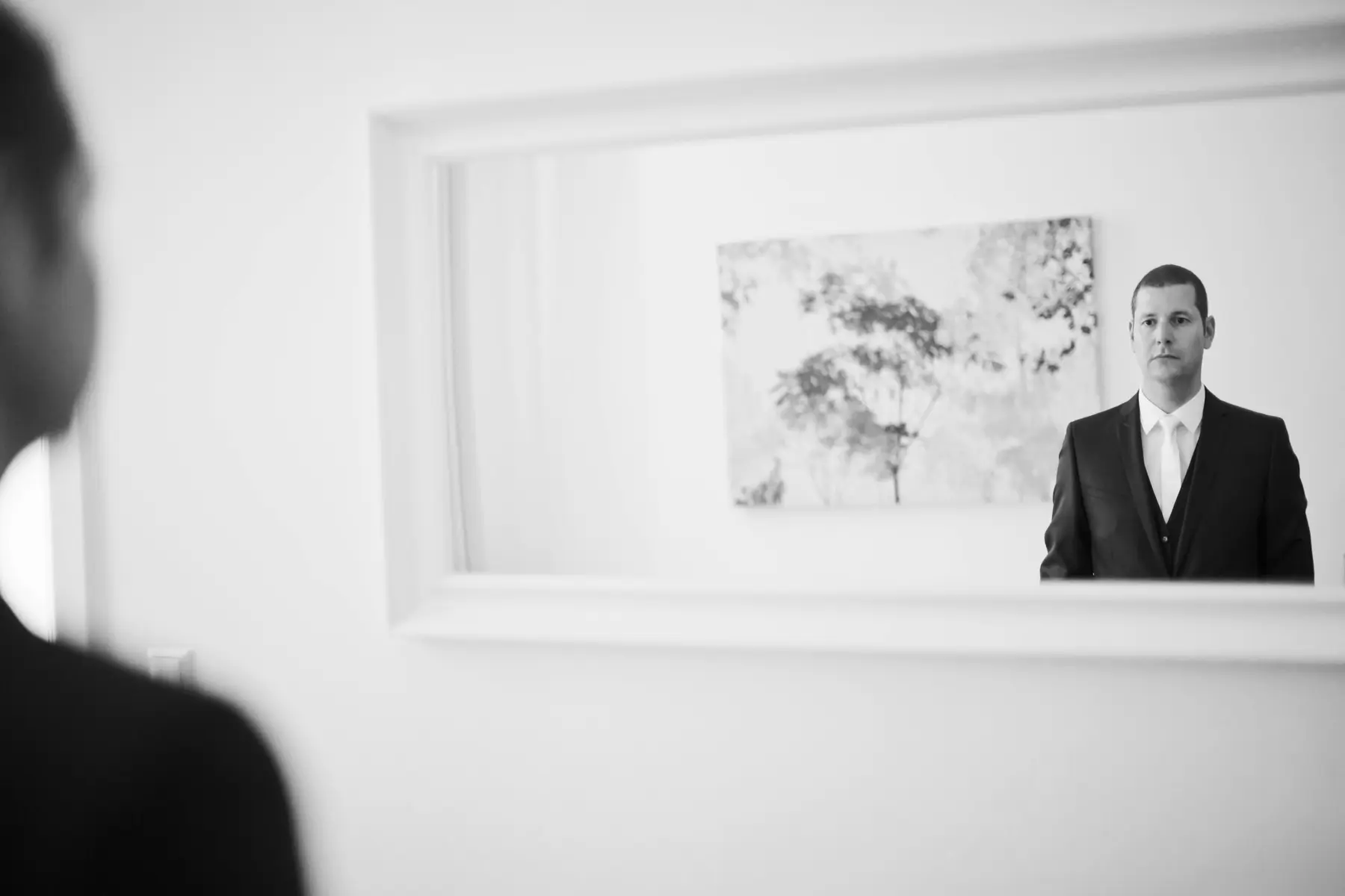 A man in a suit looks directly at the camera in a mirror reflection.