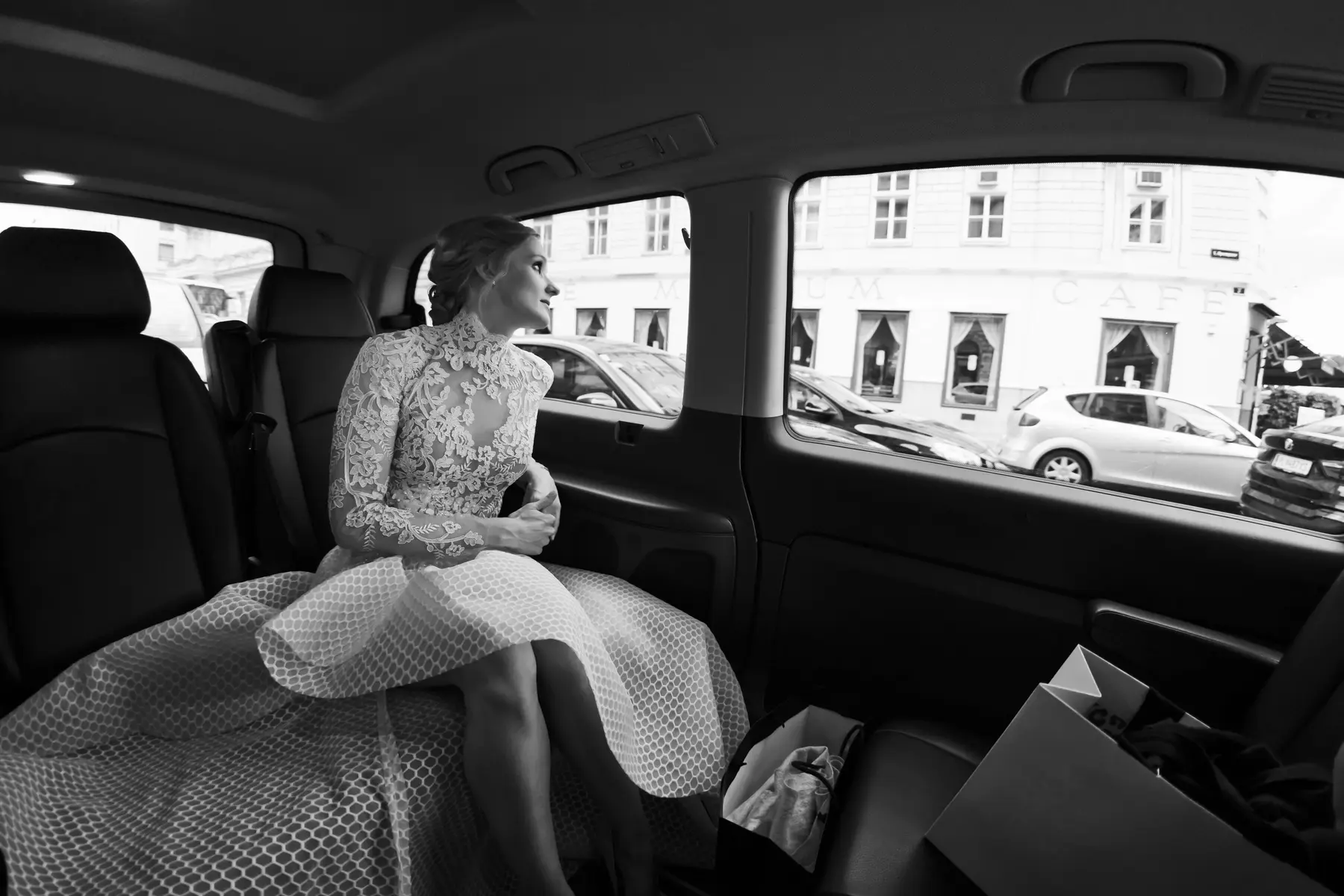 Photojournalistic photographer Vienna. A woman in a white lace dress sits in the back seat of a car, looking out the window.