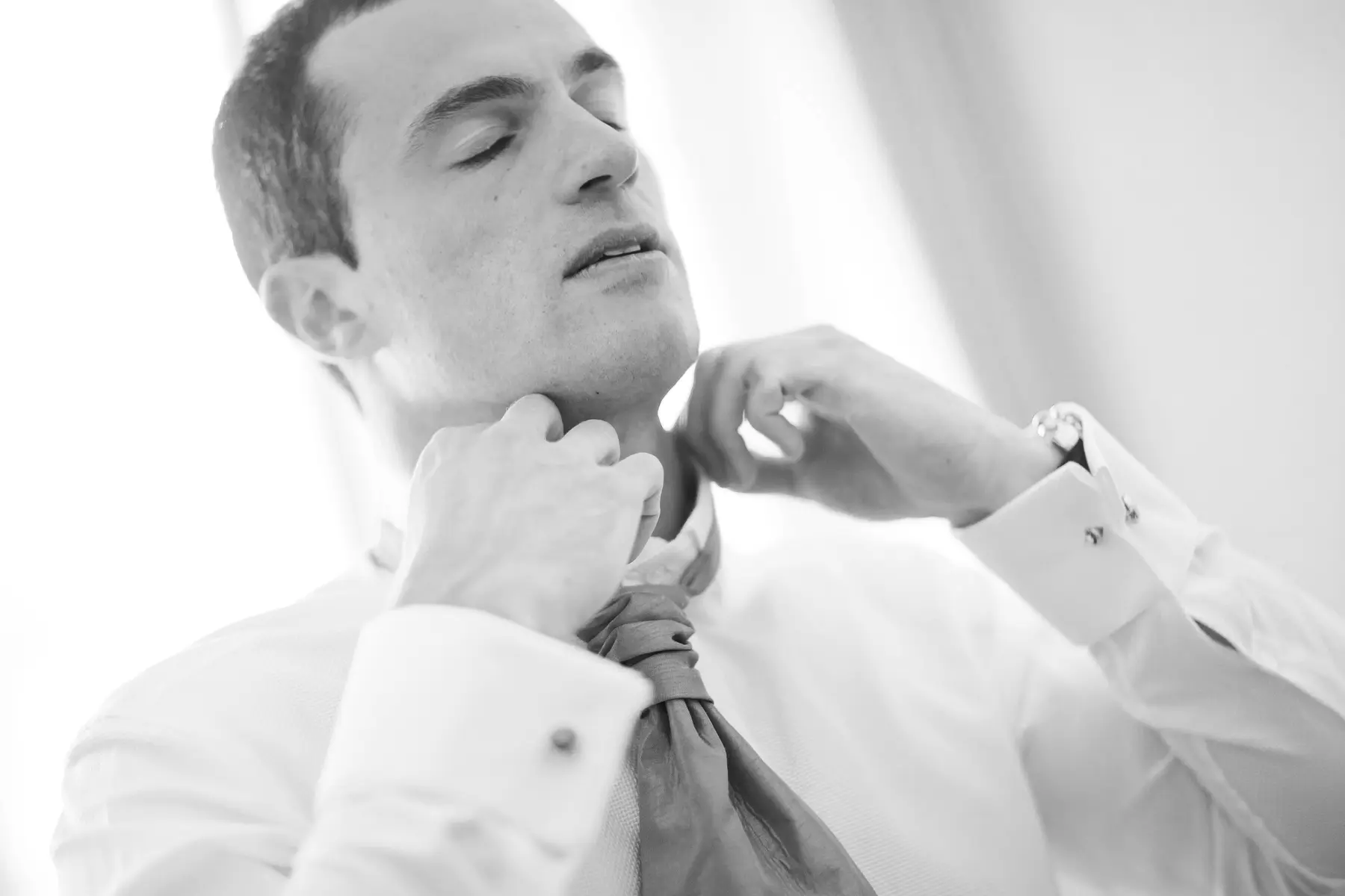 Candid shot of a groom adjusting his tie, natural wedding photography.