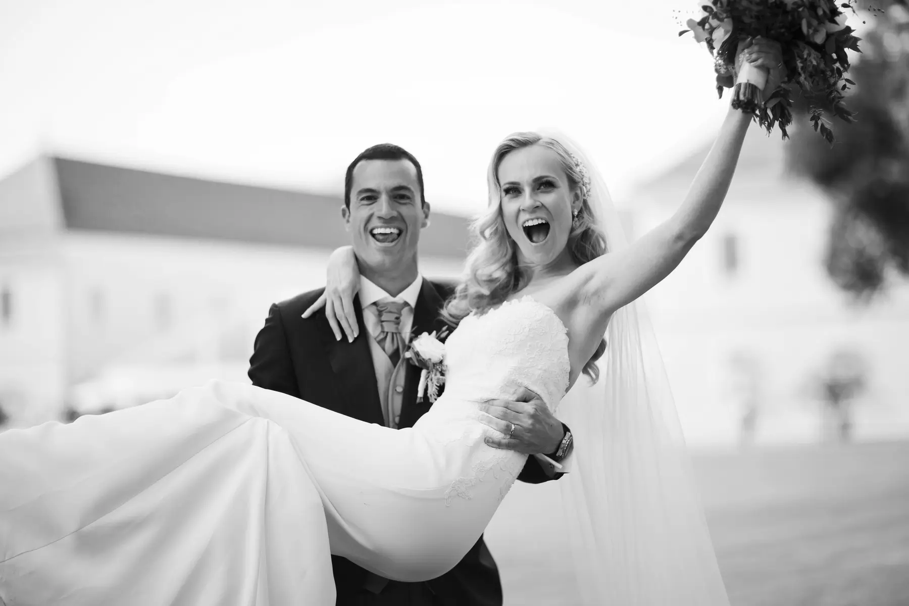 Fun and romantic shot of a groom carrying his bride in his arms, natural wedding photography Slovakia.