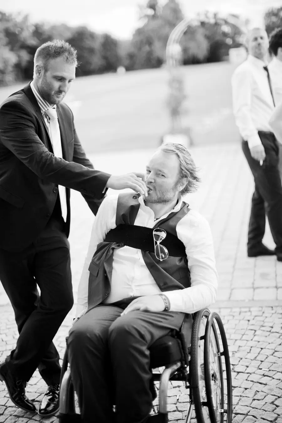 A funny candid moment of a guest in a wheelchair being helped by a friend during the wedding celebration.