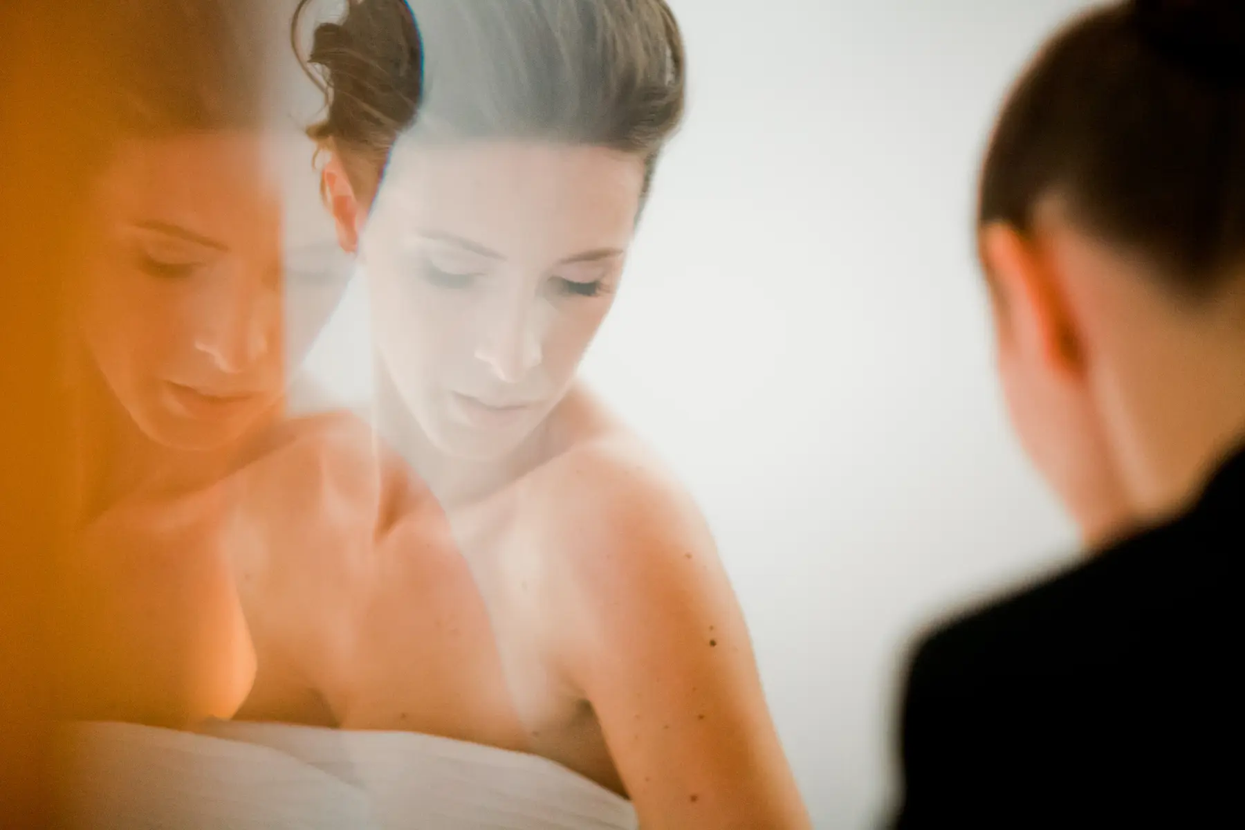 An artistic portrait of a woman, featuring a multi-exposure or reflection effect. Her head is tilted down with a contemplative expression. On the left, a warm, orange-toned,