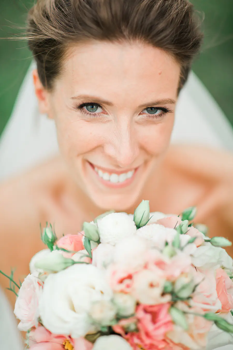 A close-up shot of a bride smiling at the camera while holding a bouquet of pink and white flowers.