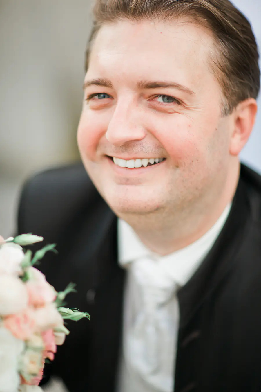 Groom smiling, holding a bouquet, in a suit.