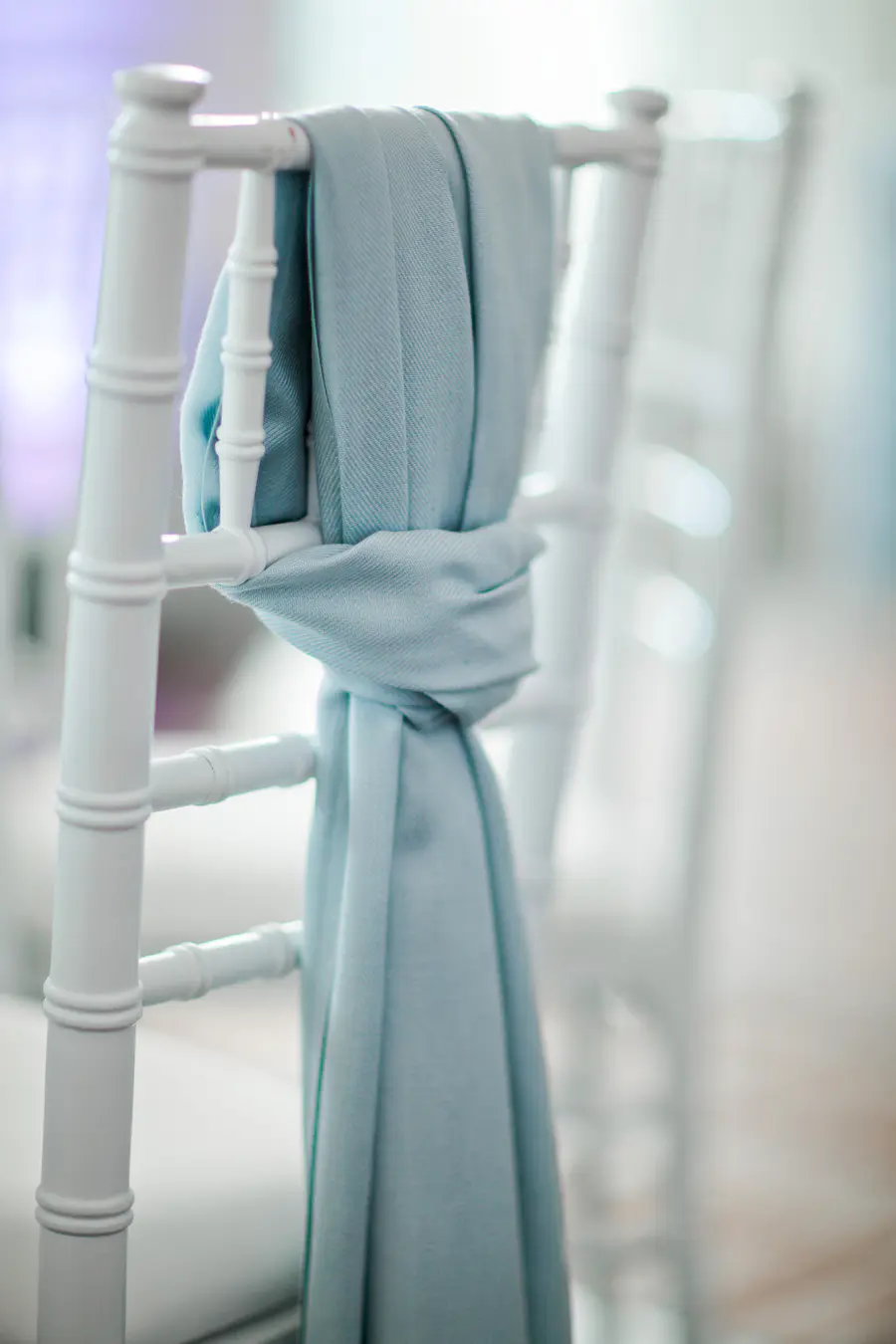 A soft pastel blue scarf elegantly draped over a wedding chair, creating a delicate and romantic atmosphere in a luxury wedding setting.