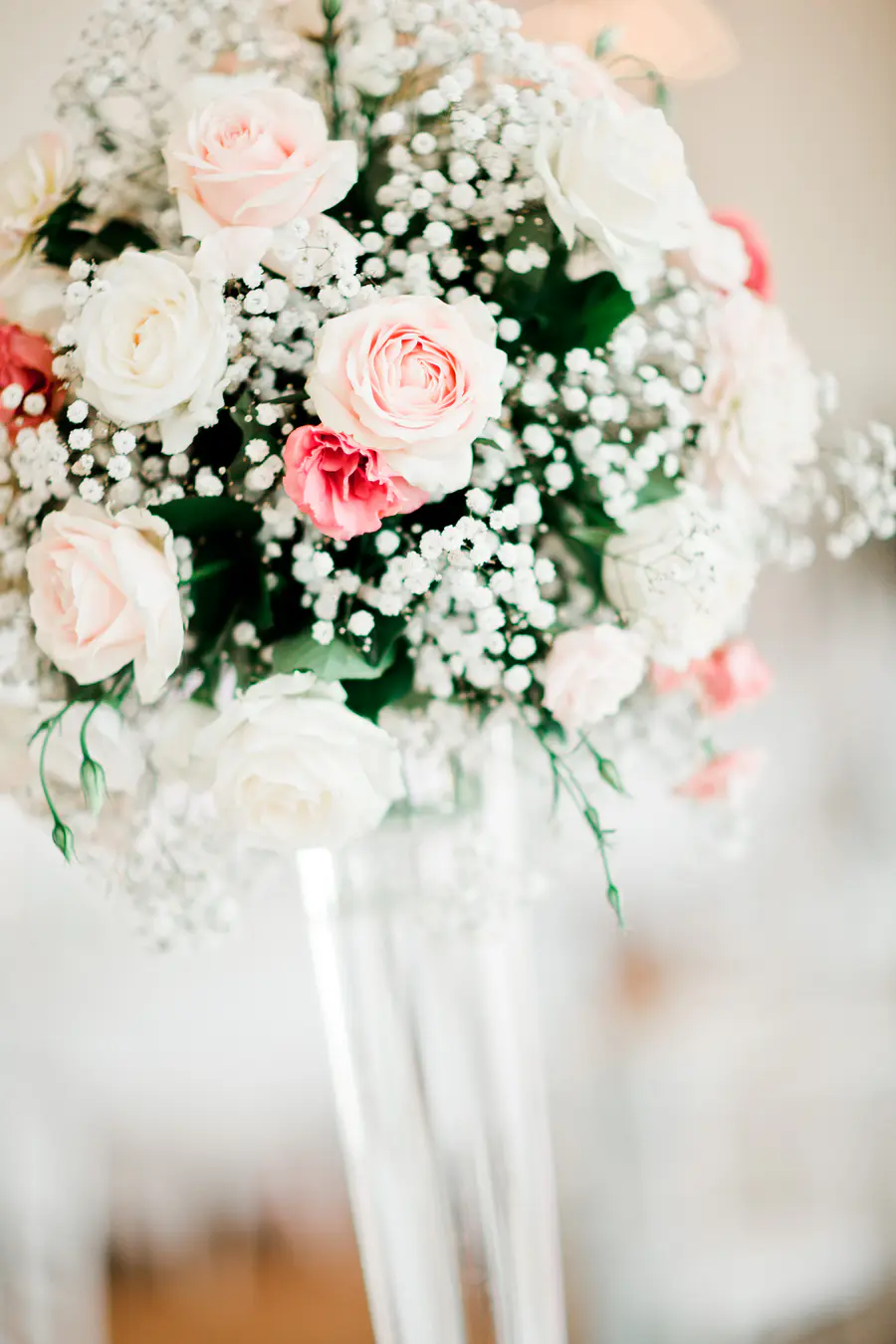 A sophisticated tall wedding bouquet featuring long-stemmed white lilies and pastel roses in a sleek glass vase, perfect for high-ceiling venue decor.