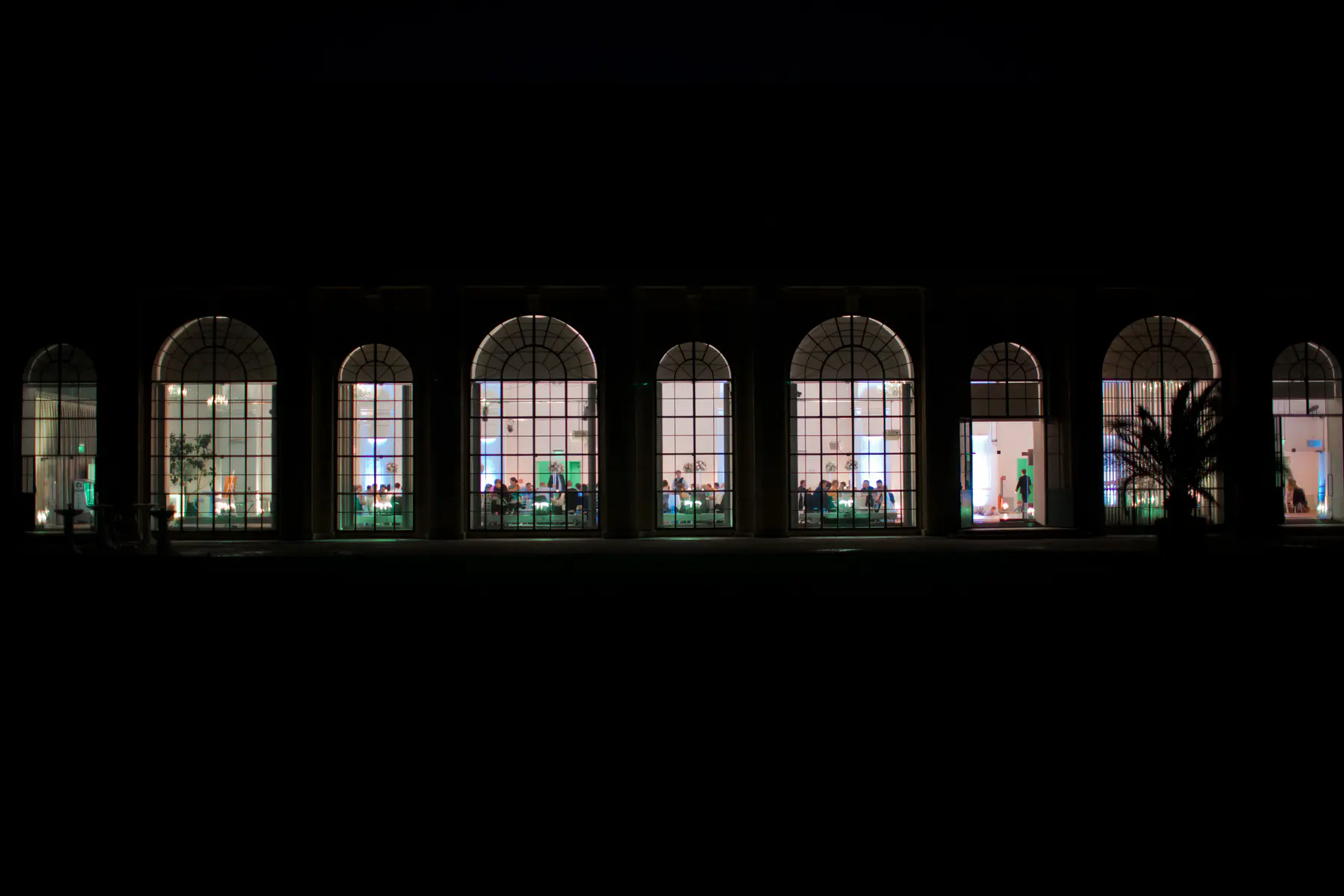An exterior perspective of the lit-up Orangery in Vienna during a wedding, capturing the contrast between the dark gardens and the vibrant party inside.