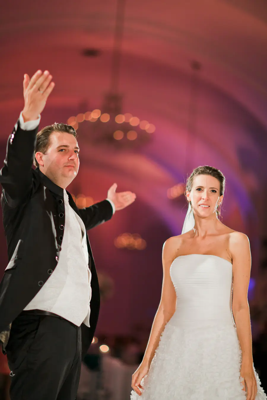 The groom raises his hands in a celebratory gesture after the dance, set against the stunning historic architecture of the Schönbrunn Orangery in Vienna.