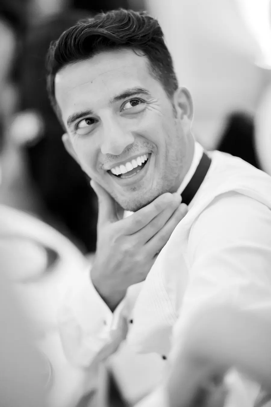  soulful black and white photograph of a smiling young man listening to wedding speeches, capturing a genuine moment of joy and emotion.